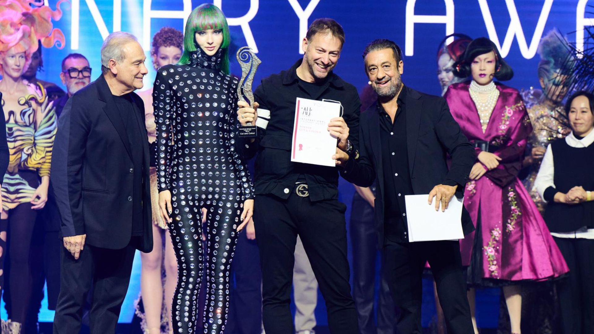 Matteo Susini premiato sul palco del Visionary Award 2024, affiancato da una modella con i capelli verde lime e altri partecipanti, mentre riceve il trofeo per la categoria Cut and Color.