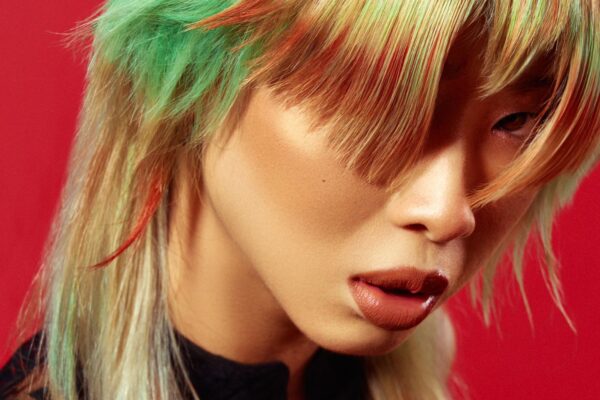 Modello con capelli multicolore in stile manga, con tonalità verde e rosso, su sfondo rosso.