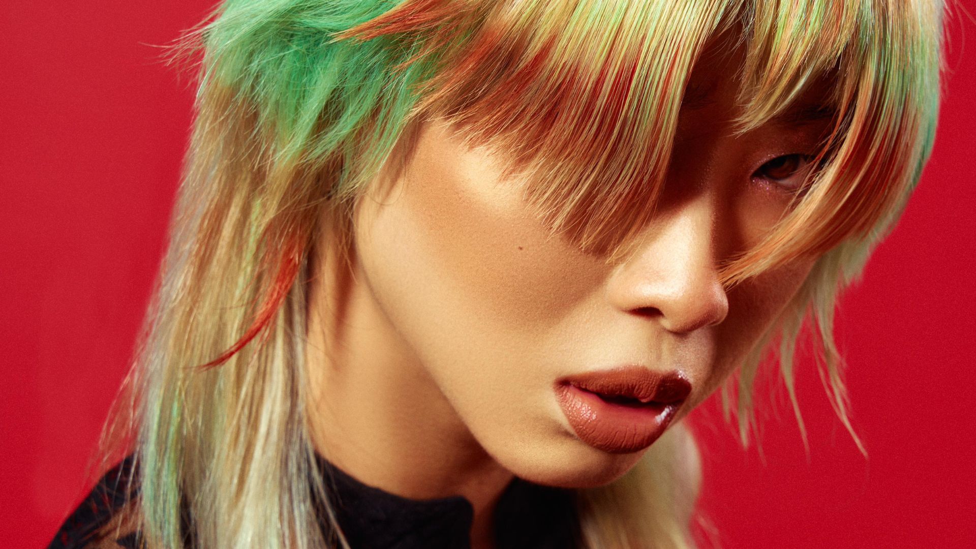 Modello con capelli multicolore in stile manga, con tonalità verde e rosso, su sfondo rosso.