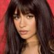 Camila Cabello con un long bob castano cioccolato, frangia piena e morbida, su sfondo rosso.