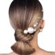 Acconciatura Sleek Bow Bun con effetto ultra liscio e decorata con perle di diverse dimensioni, elegante e sofisticata.