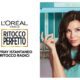Donna con capelli scuri e lucenti tiene in mano uno spray L'Oréal Paris Ritocco Perfetto, con uno sguardo sicuro e soddisfatto.