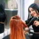 Parrucchiera sorridente mentre asciuga i capelli a una cliente con una spazzola tonda e un phon.