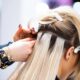 Applicazione di extensions adesive su capelli biondi in un salone professionale. Una hairstylist utilizza clip per sezionare i capelli e fissare le ciocche con la tecnica tape-in, creando un effetto naturale e voluminoso.