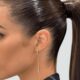 Primo piano di una donna con capelli raccolti in una sleek ponytail, una coda di cavallo alta, liscia e ultra brillante. Il look sofisticato è completato da un orecchino lungo e un trucco naturale.