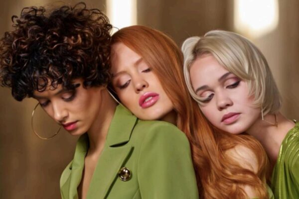 Tre modelle con capelli ricci, rossi lisci e biondi scalati in uno shooting professionale, indossando abiti verde oliva.