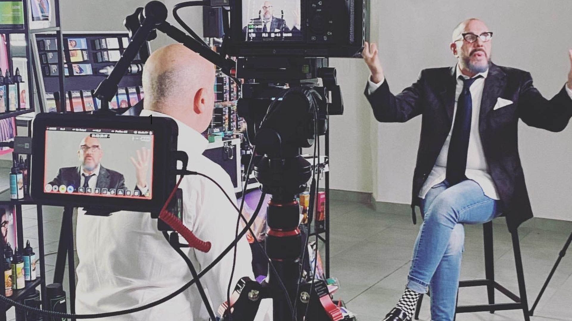 Intervista in studio con esperto del settore beauty davanti a telecamere e scaffali di prodotti cosmetici.