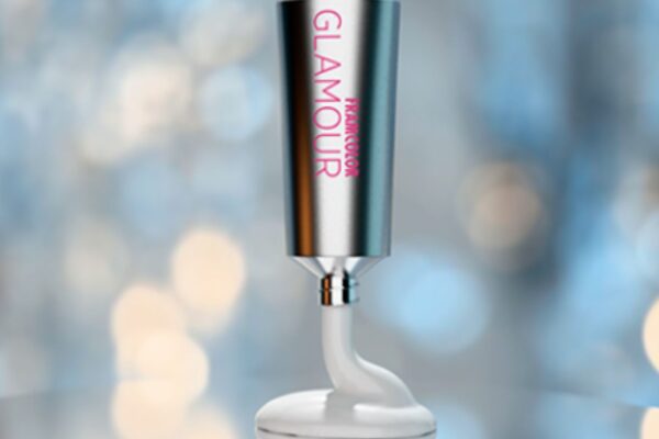 Tubo di colore professionale Framcolor Glamour di Framesi, in metallo satinato, con prodotto bianco in uscita, su sfondo sfocato blu