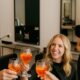 Parrucchiere e clienti in salone moderno mentre brindano con uno spritz