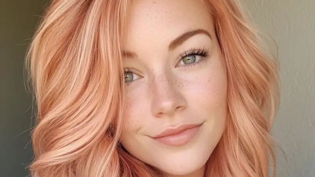 Primo piano di una donna con capelli color peach blonde, pelle chiara e occhi verdi, pettinatura mossa e luminosa.