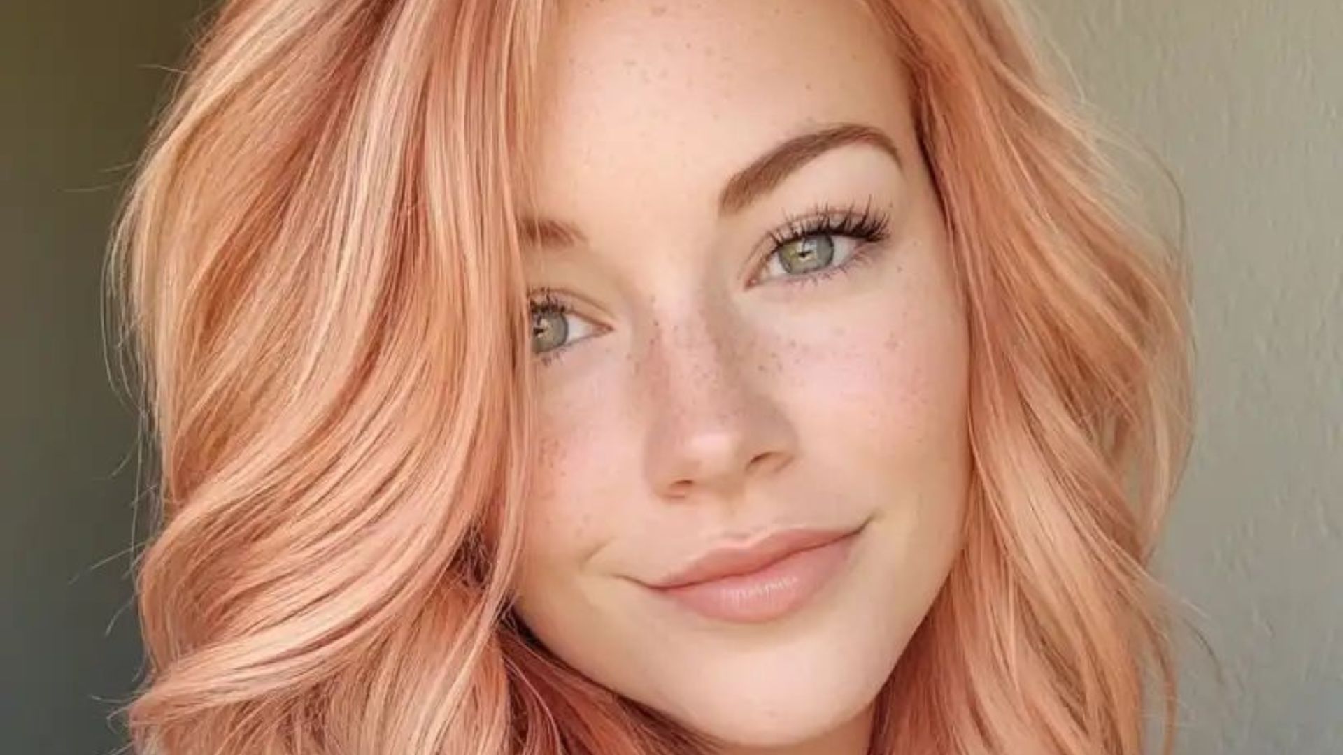 Primo piano di una donna con capelli color peach blonde, pelle chiara e occhi verdi, pettinatura mossa e luminosa.