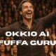 Uomo in camicia che parla a una folla adorante con la scritta “OKKIO AI FUFFA GURU!”