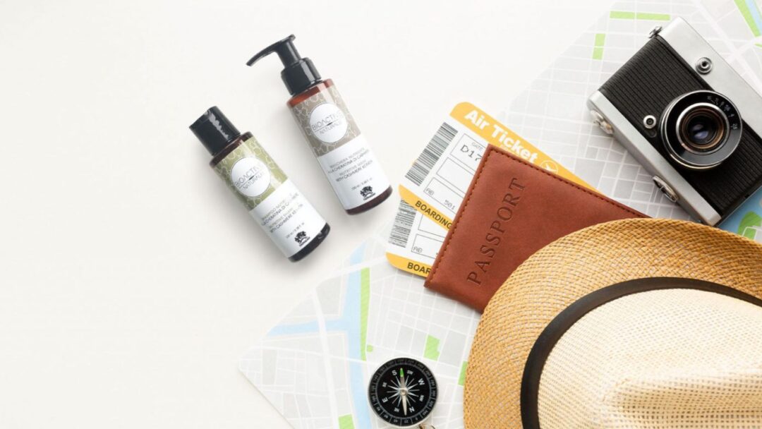 Travel kit Farmagan con shampoo e maschera in formato mini, affiancati da passaporto, biglietti aerei e fotocamera su sfondo chiaro.