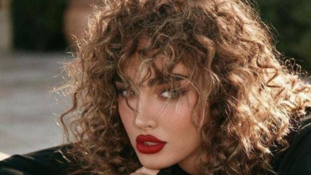 Donna con capelli ricci naturali ben definiti e labbra rosse, simbolo della bellezza curly 2025