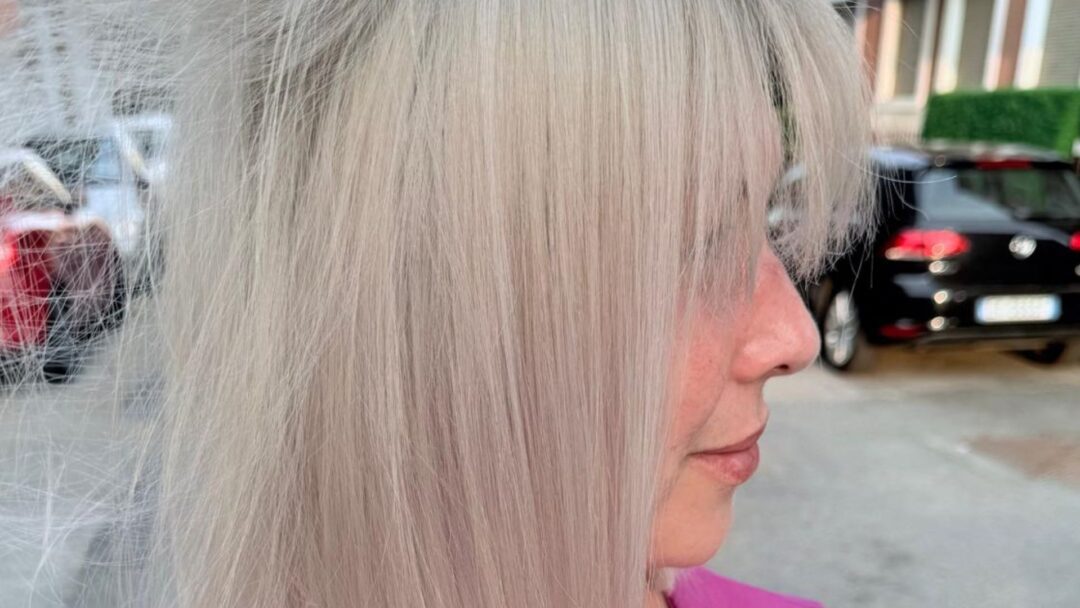 Primo piano laterale di capelli biondo perla lisci e luminosi su donna con frangia, realizzati in salone