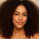 Modella con capelli ricci naturali ben definiti, pelle mulatta e look semplice su sfondo beige