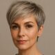Donna over 40 con taglio pixie silver-blonde e frangia morbida laterale, sguardo sicuro, sfondo beige neutro.