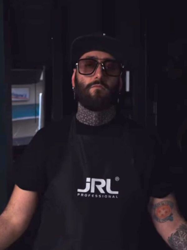 Hair stylist con grembiule JRL Professional in posa frontale, ambiente interno con luce soffusa