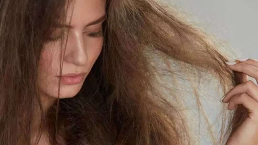 Donna con capelli visibilmente danneggiati e crespi, che osserva le lunghezze rovinate