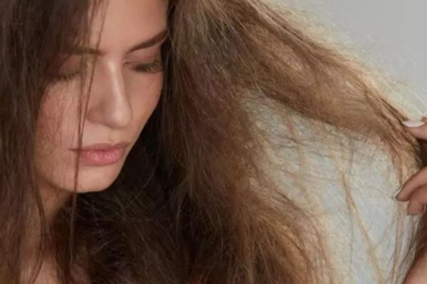 Donna con capelli visibilmente danneggiati e crespi, che osserva le lunghezze rovinate