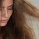 Donna con capelli visibilmente danneggiati e crespi, che osserva le lunghezze rovinate