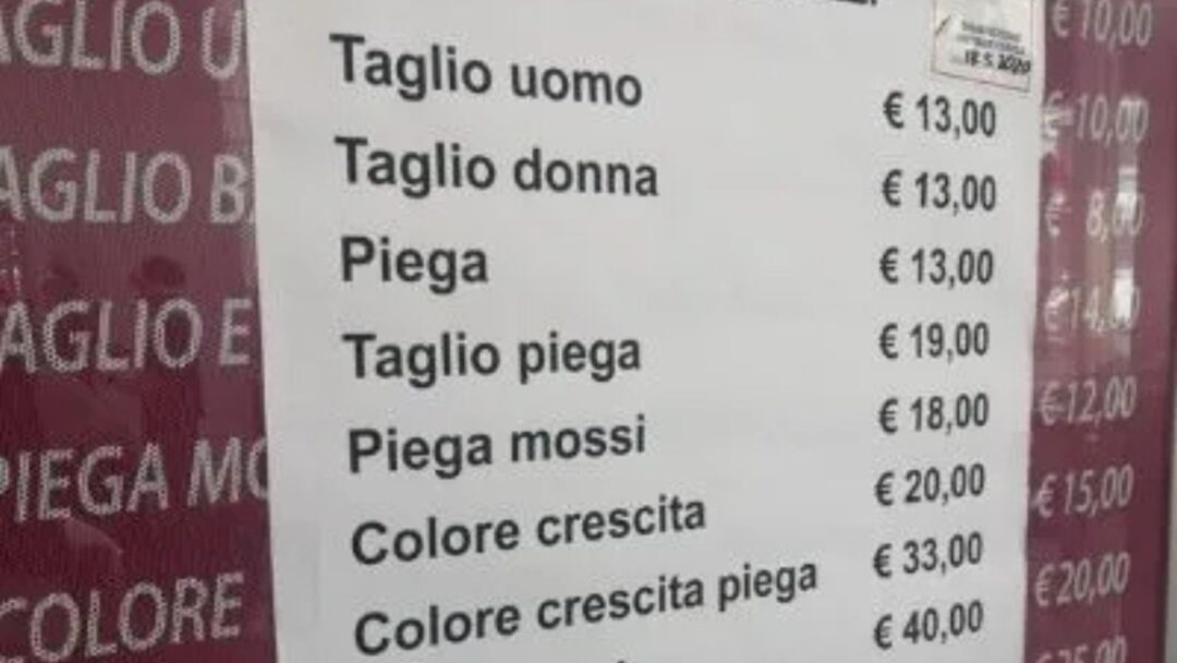 Listino prezzi esposto fuori da un salone di parrucchiere italiano con servizi come taglio, piega e colore, e tariffe aggiornate al 2025.