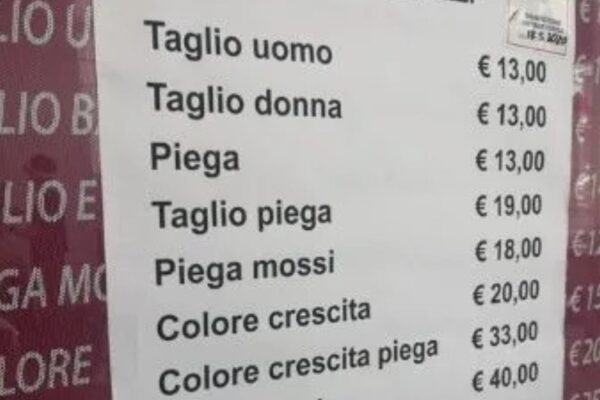 Listino prezzi esposto fuori da un salone di parrucchiere italiano con servizi come taglio, piega e colore, e tariffe aggiornate al 2025.