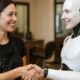 Parrucchiera e robot umanoide che si stringono la mano sorridendo all’interno di un salone, simbolo di collaborazione tra uomo e intelligenza artificiale