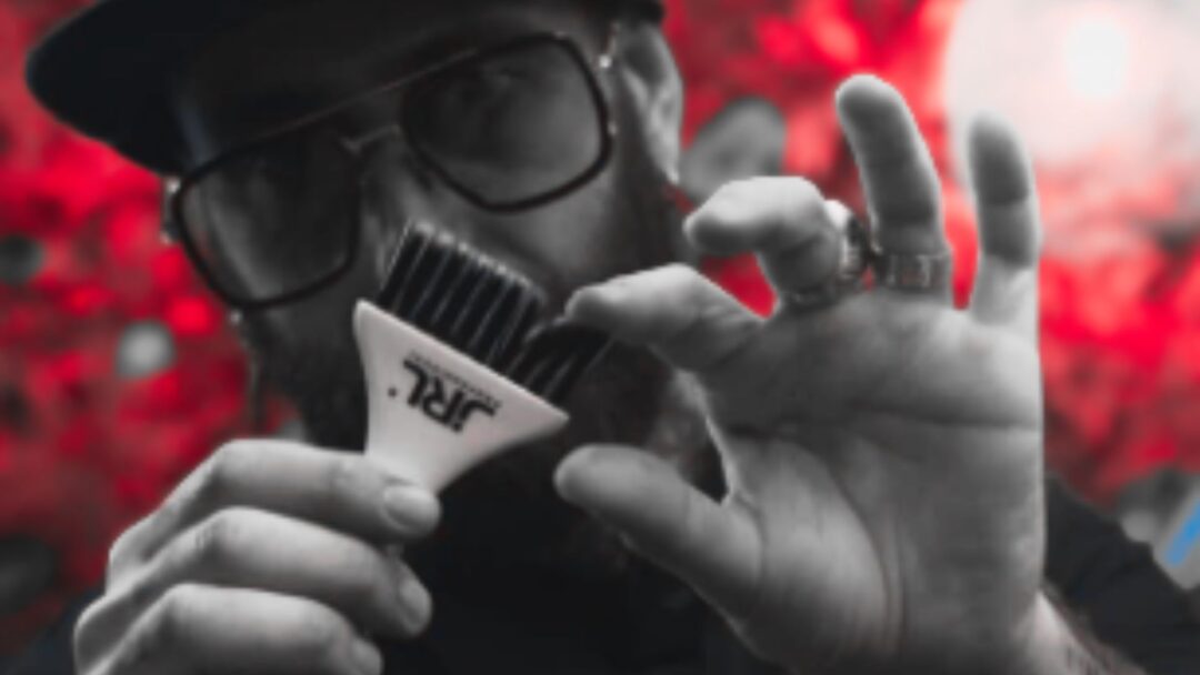 Hair stylist mostra accessorio JRL Professional in primo piano, con sfondo rosso sfocato