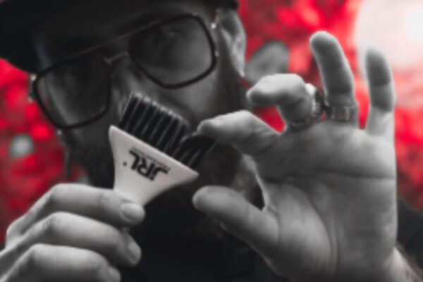 Hair stylist mostra accessorio JRL Professional in primo piano, con sfondo rosso sfocato
