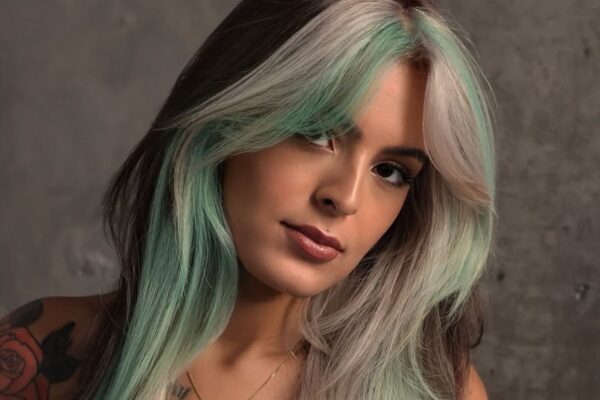 Donna con capelli lunghi color menta, cioccolato e biondo freddo, taglio scalato con curtain bangs, su sfondo grigio.
