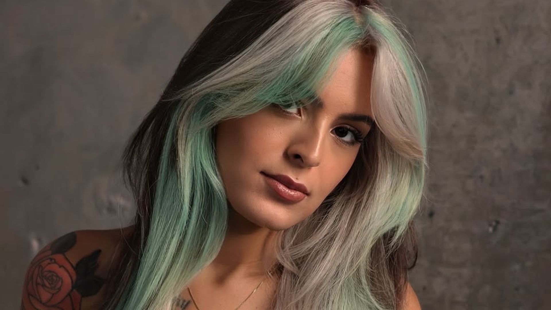 Donna con capelli lunghi color menta, cioccolato e biondo freddo, taglio scalato con curtain bangs, su sfondo grigio.