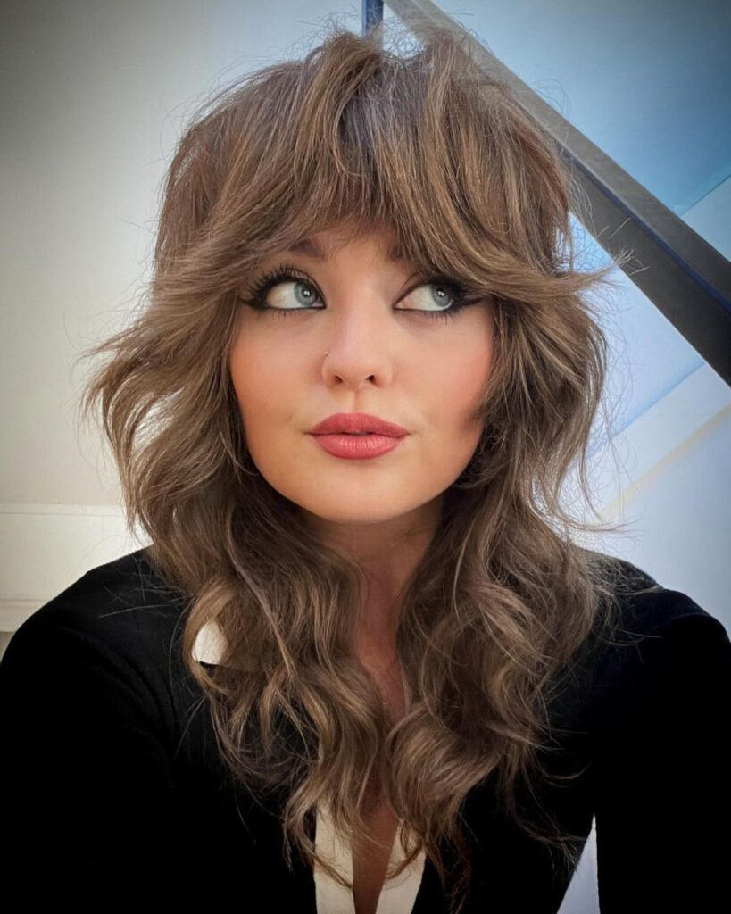 Donna con taglio shag medio lungo e frangia piena, stile anni ’70 rivisitato in chiave moderna, tendenza capelli 2025.
