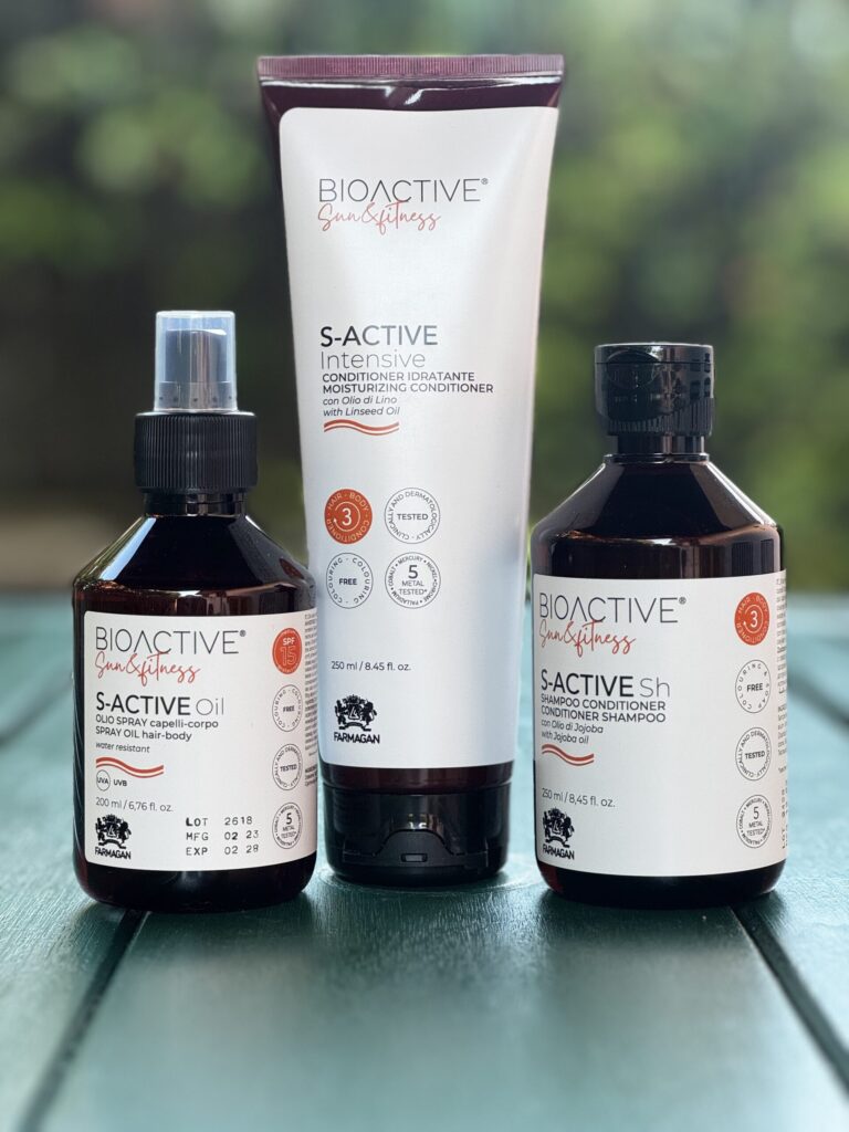 Prodotti solari professionali Farmagan Bioactive Sun & Fitness: olio spray, conditioner e shampoo esposti su tavolo all’aperto