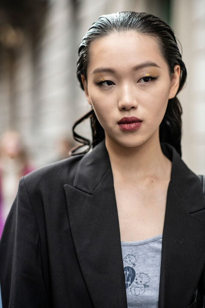 Donna con pettinatura effetto wet look e trucco grafico dorato, tendenza capelli e makeup estate 2025.