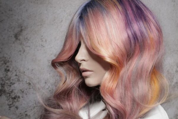 Capelli lunghi ondulati con sfumature rosa, viola, arancio e giallo, realizzati da Stefano Bugada per il progetto OVERLAPS di Hairtium.