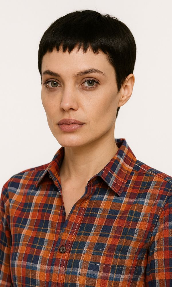 Modella con Pixie Cut baby bang 2025, frangia cortissima e capelli scuri, camicia a quadri stile Dsquared, scatto in studio.