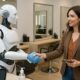 Donna stringe la mano a un robot receptionist in un salone moderno, simbolo di igiene, tecnologia e futuro dell’esperienza cliente.