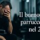 Parrucchiere seduto con la testa bassa, in un salone sfocato, mentre mostra segni di stanchezza. Testo sovrapposto: “Il burnout dei parrucchieri nel 2025”.