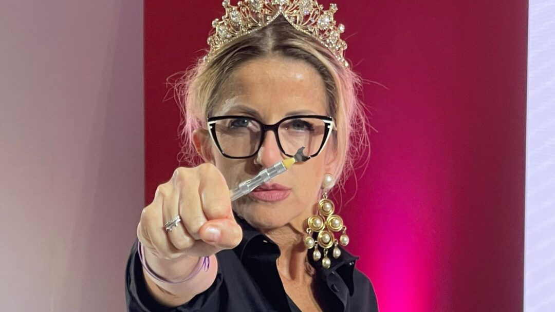 Hairstylist con corona e occhiali punta verso la camera uno strumento tecnico per capelli durante una dimostrazione.