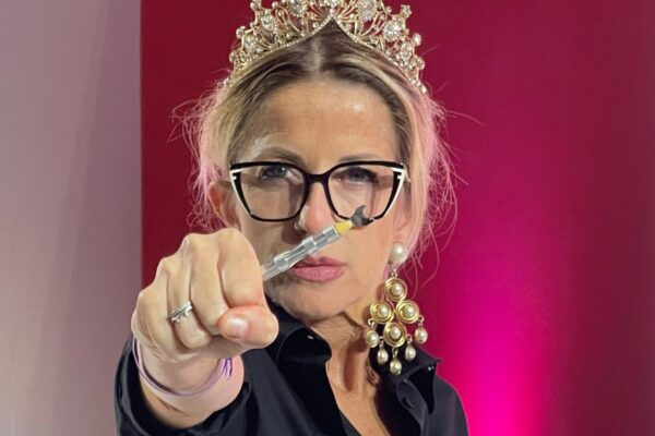 Hairstylist con corona e occhiali punta verso la camera uno strumento tecnico per capelli durante una dimostrazione.