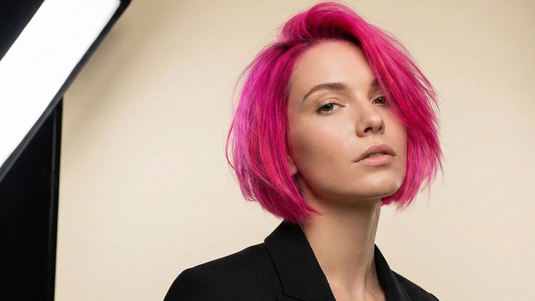 Modella con taglio bob e colore Neon Pulse fucsia acceso, abito nero elegante, fotografata in studio con fondo chiaro e luci professionali.