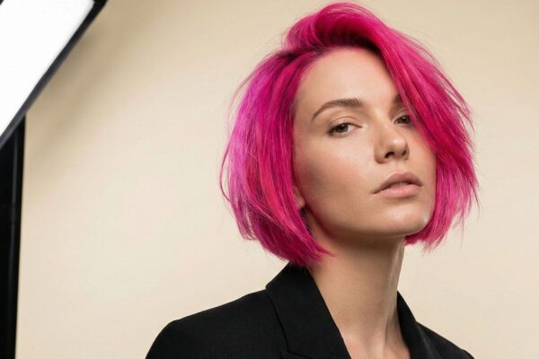 Modella con taglio bob e colore Neon Pulse fucsia acceso, abito nero elegante, fotografata in studio con fondo chiaro e luci professionali.
