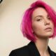 Modella con taglio bob e colore Neon Pulse fucsia acceso, abito nero elegante, fotografata in studio con fondo chiaro e luci professionali.