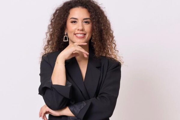 Ritratto professionale di una giovane donna con capelli ricci e castani, che sorride con sicurezza indossando un blazer nero su sfondo bianco.