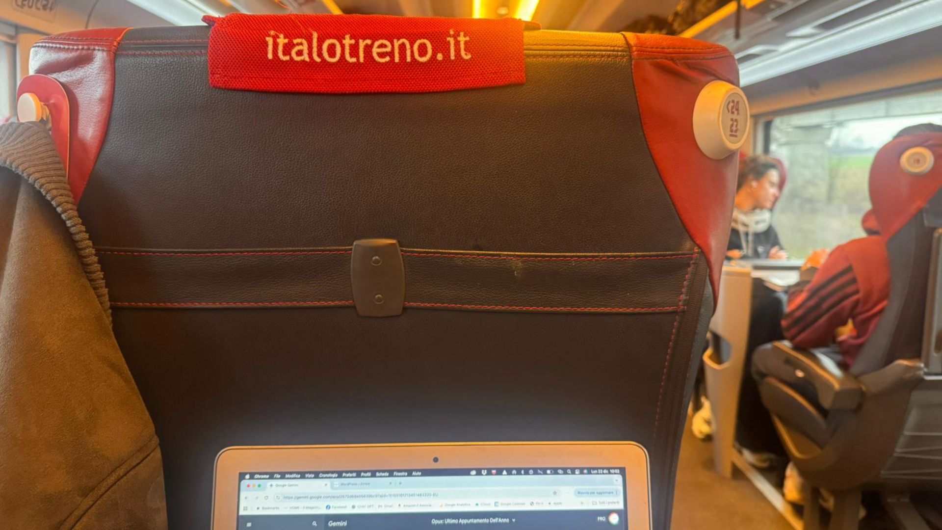 L'interno di una carrozza ferroviaria Italo con un laptop aperto sul tavolino, che mostra una pagina web. Il sedile anteriore ha un poggiatesta rosso con il logo "italotreno.it".
