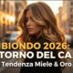 Immagine di copertina con una donna dai capelli balayage miele e oro al tramonto in città. Testo sovrapposto: "BIONDO 2026: IL RITORNO DEL CALDO - Tendenza Miele & Oro".