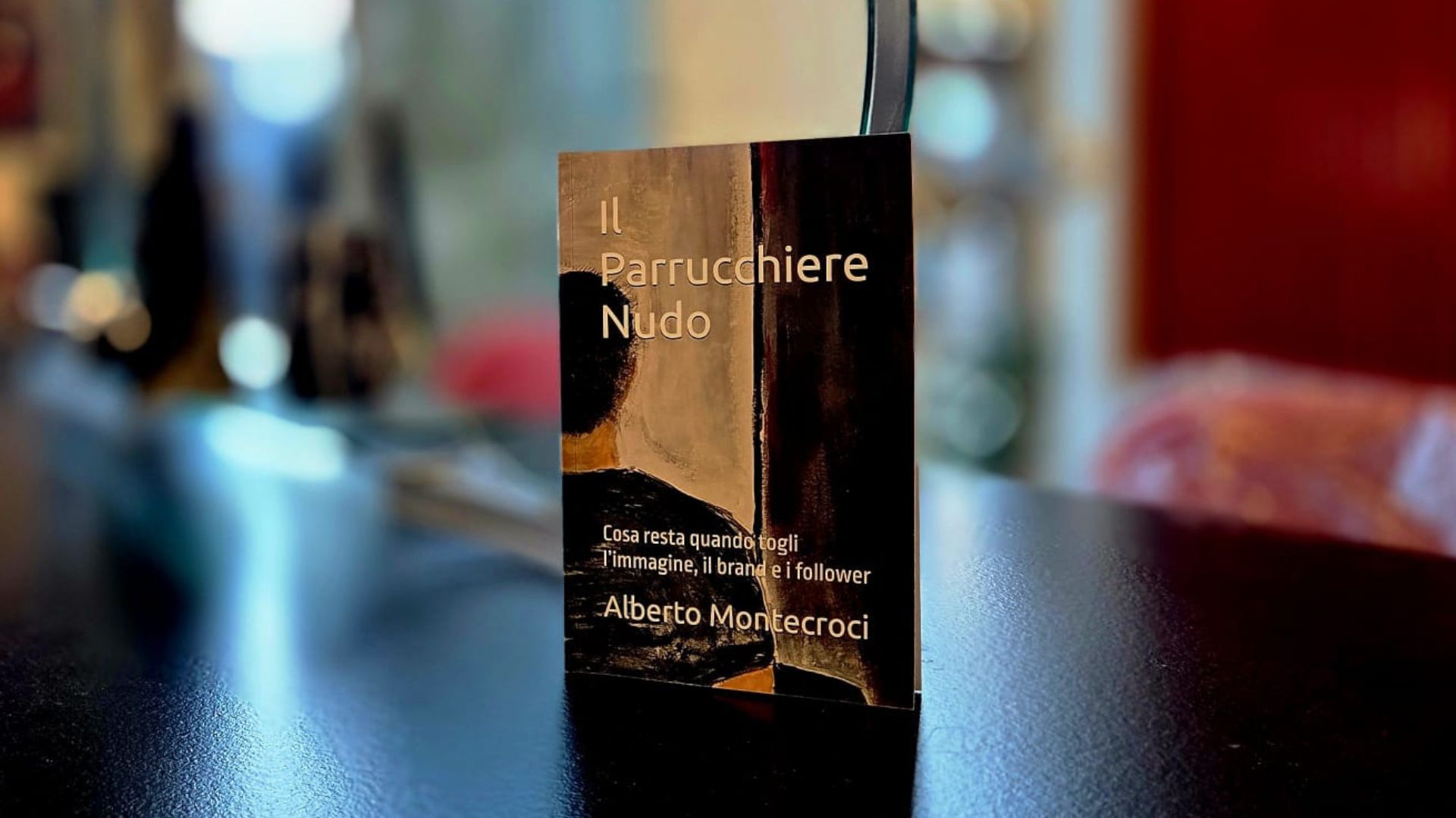 Libro “Il Parrucchiere Nudo” di Alberto Montecroci appoggiato su un tavolo in salone, con sfondo sfocato e luci calde.