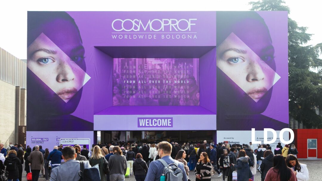 Ingresso principale della fiera Cosmoprof Worldwide Bologna con grande folla di visitatori e banner viola.
