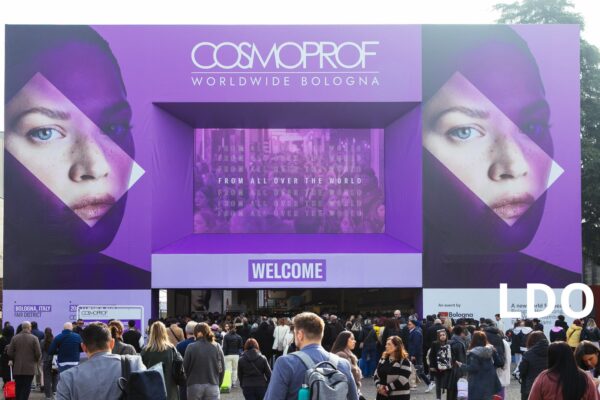 Ingresso principale della fiera Cosmoprof Worldwide Bologna con grande folla di visitatori e banner viola.